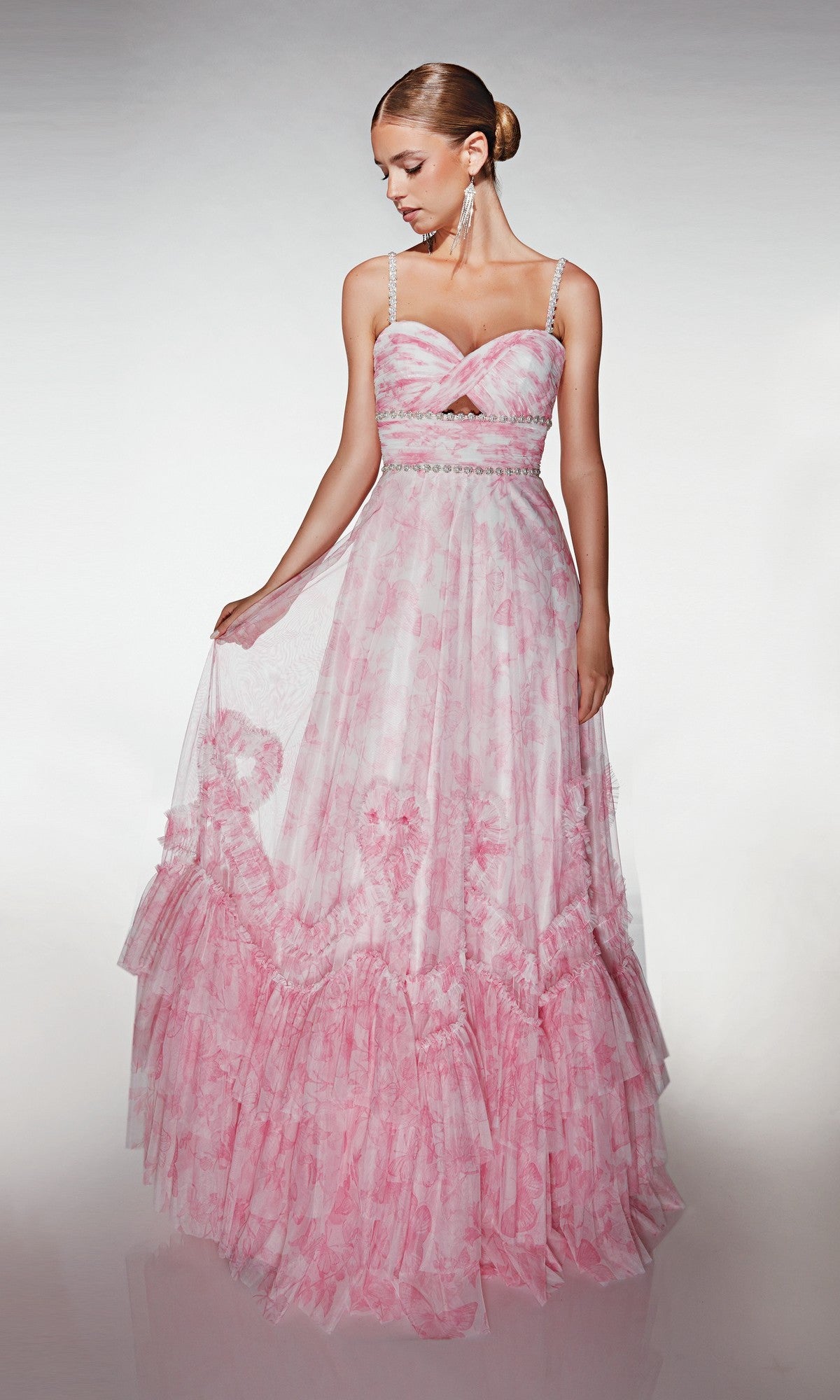 Model showcases the Alyce 62063, a long formal dress in light pink floral print with thin straps, holding out the skirt against a plain background.